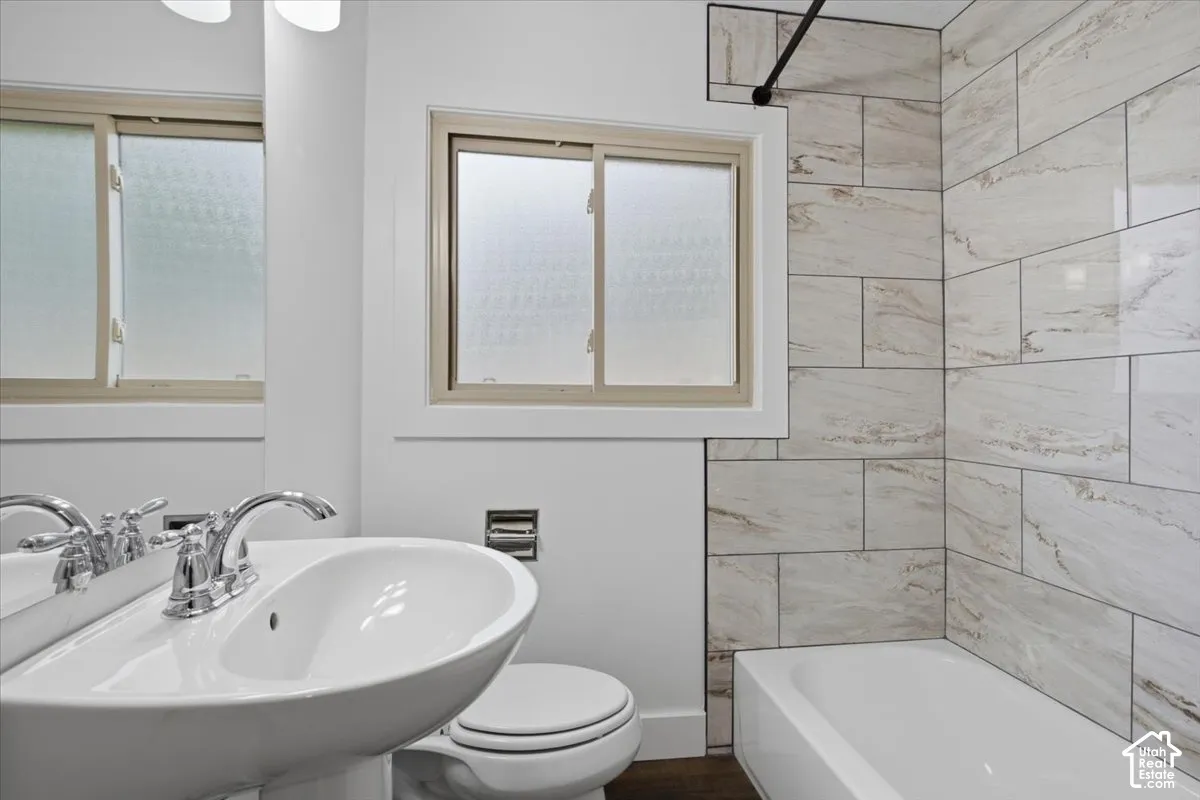 Pedestal sink with chrome faucet, white porcelain toilet, built-in bathtub, and large format wall tiling