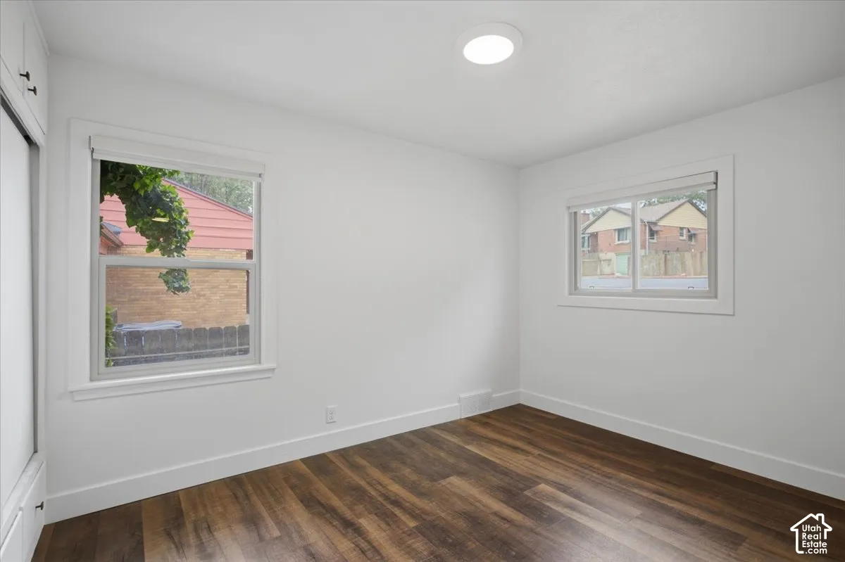 Wood-finish flooring with white baseboards, two windows with white trim, and a built-in closet with white doors