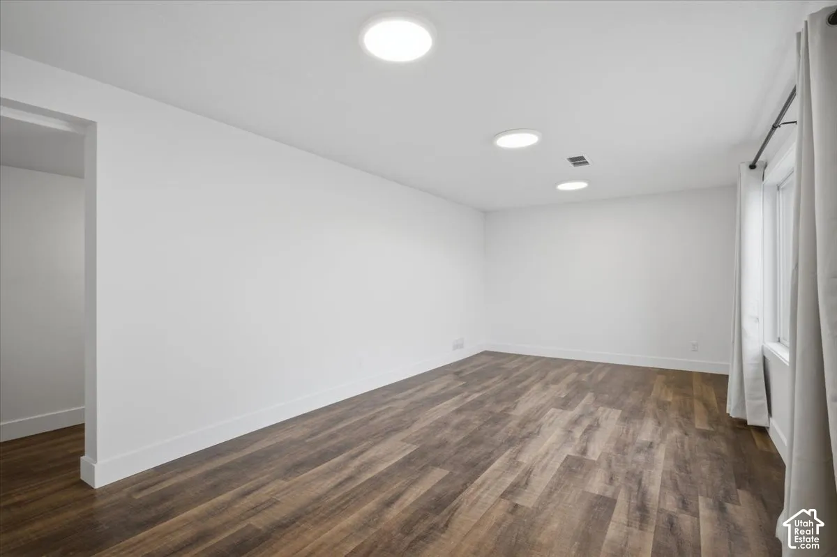 Recessed lighting, wood-finish flooring, white walls, and a window with a curtain rod