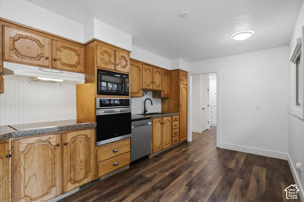 Wood-finish flooring, built-in stainless steel appliances, granite-style countertops, wood cabinetry, and a black gooseneck faucet