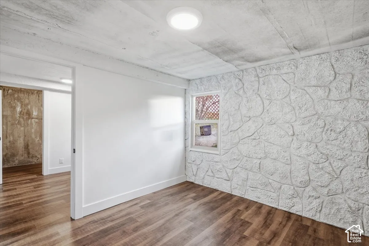 Wood-finish flooring with a white textured accent wall, recessed lighting, and a window providing natural illumination