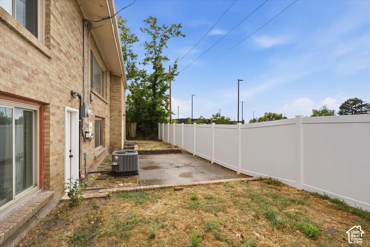 Brick exterior, white vinyl fencing, concrete patio area, and exterior utility access