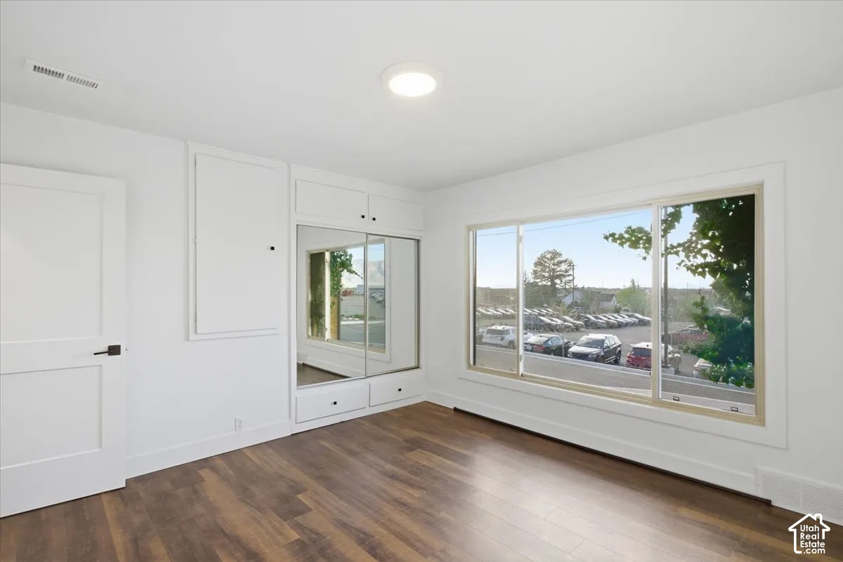 Wood-finish flooring, built-in storage with mirrored closet doors, and large windows with white trim
