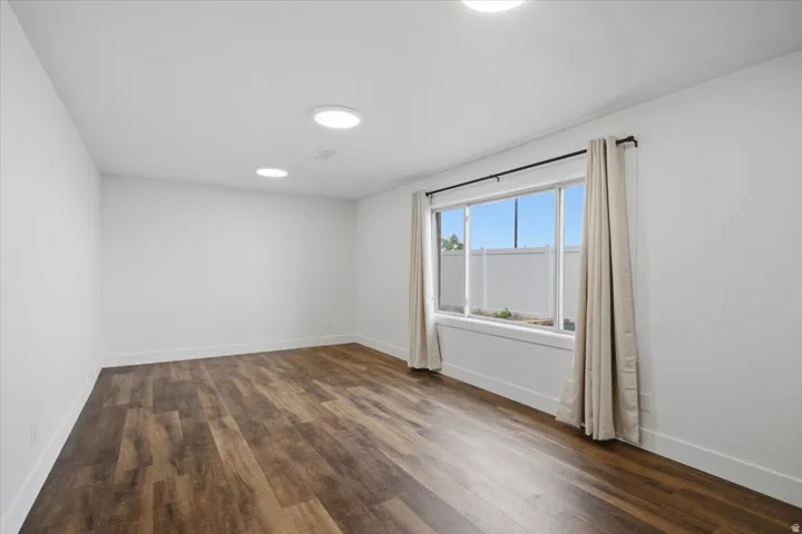 Recessed lighting, wood-finish flooring, white walls, and a large window with window treatments
