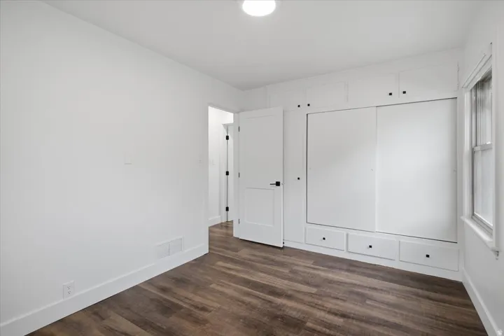 Built-in white cabinetry with sliding doors and drawer storage, wood-finish flooring, white trim, and a window