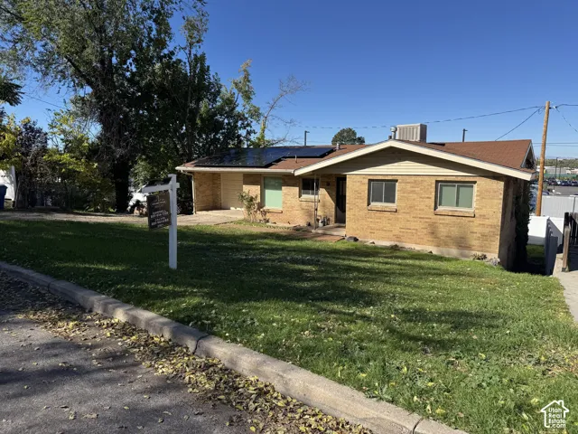 Single-story brick exterior featuring a shingle roof, integrated solar panels, and a concrete driveway