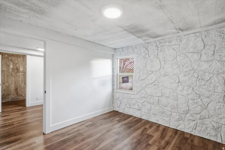 Wood-finish flooring with a white textured accent wall, recessed lighting, and a window providing natural illumination
