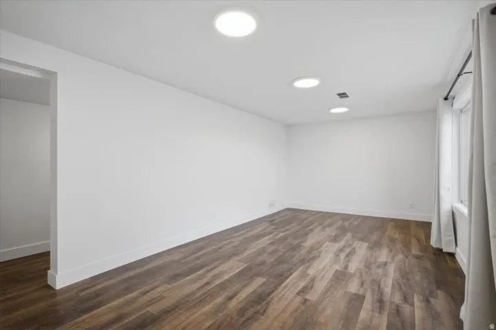 Recessed lighting, wood-finish flooring, white walls, and a window with a curtain rod
