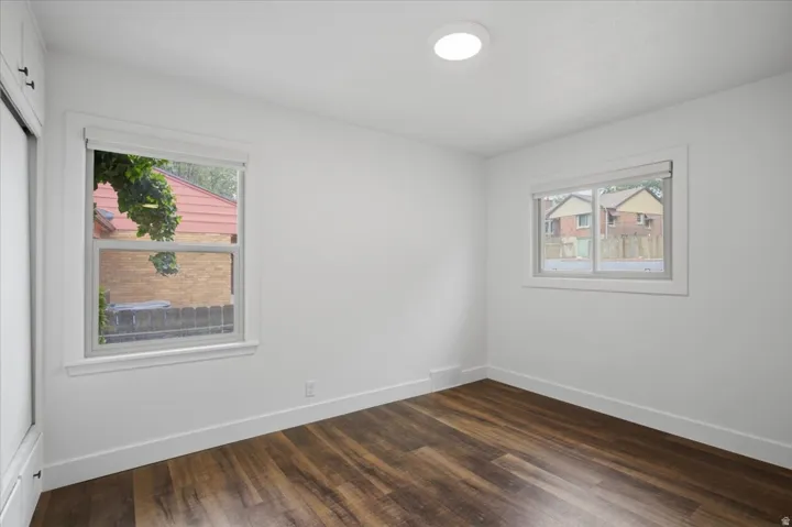 Wood-finish flooring with white baseboards, two windows with white trim, and a built-in closet with white doors