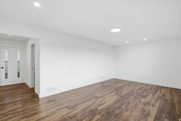 Spacious room featuring wood-finish flooring, recessed lighting, a round flush-mount ceiling light, and a white interior door with vertical glass panels
