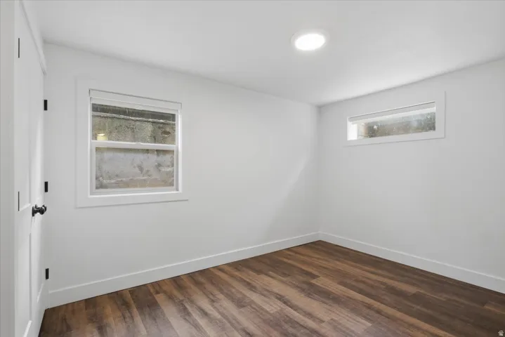 Recessed ceiling lighting, wood-finish flooring, white trim, and a white interior door with black hardware
