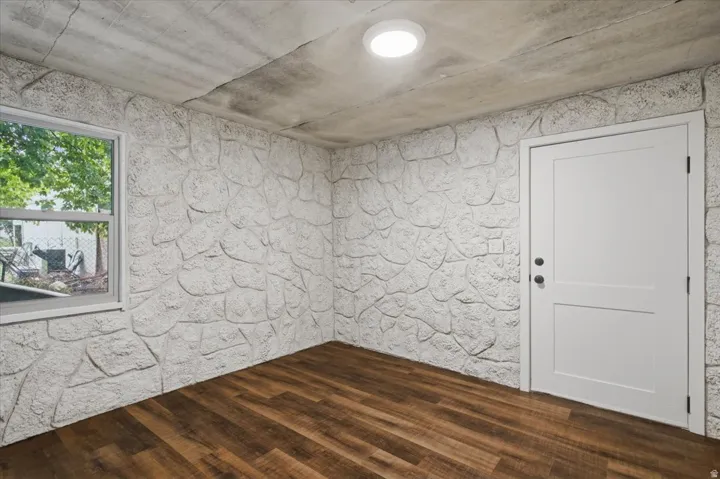 Textured stone-look wall finish, wood-finish flooring, white panel door, and white frame window