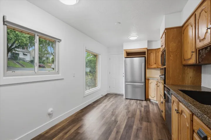 Kitchen space featuring wood-finish flooring, two large windows, wood cabinetry, granite-style countertops, and stainless steel appliances