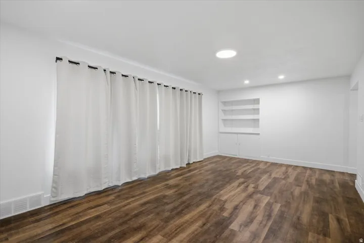 Wood-finish flooring, recessed lighting, built-in shelving, and white walls