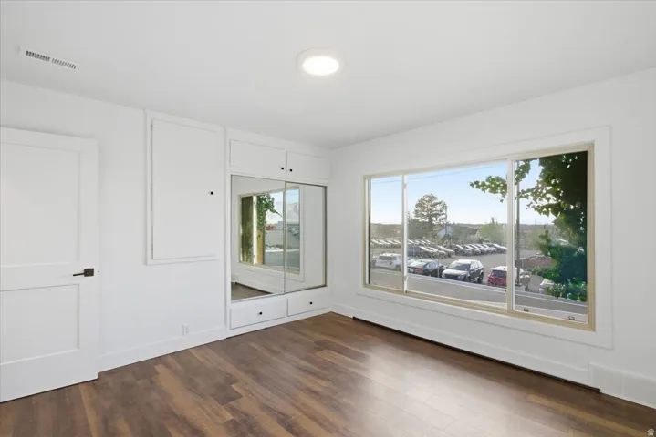 Wood-finish flooring, built-in storage with mirrored closet doors, and large windows with white trim