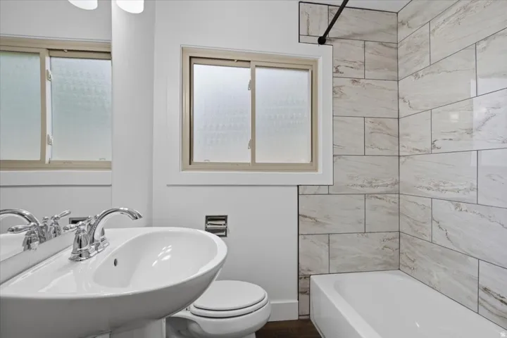 Pedestal sink with chrome faucet, white porcelain toilet, built-in bathtub, and large format wall tiling