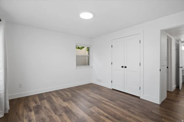 Wood-finish flooring with white baseboards, a window, and a built-in closet with panel doors