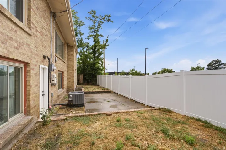 Brick exterior, white vinyl fencing, concrete patio area, and exterior utility access