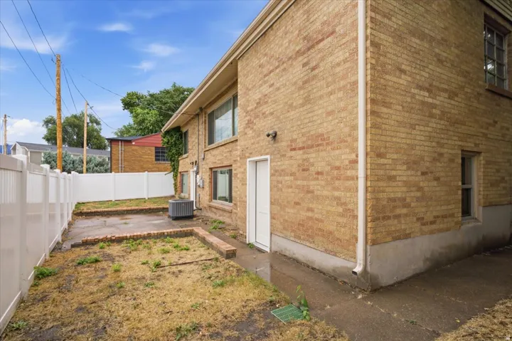 Brick exterior with multiple windows, white privacy fencing, and a concrete pathway