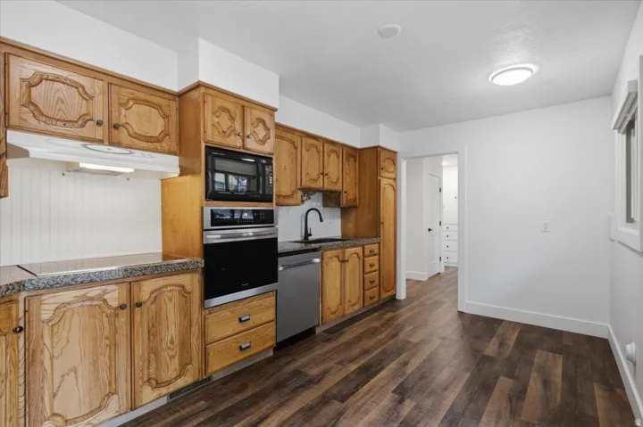 Wood-finish flooring, built-in stainless steel appliances, granite-style countertops, wood cabinetry, and a black gooseneck faucet