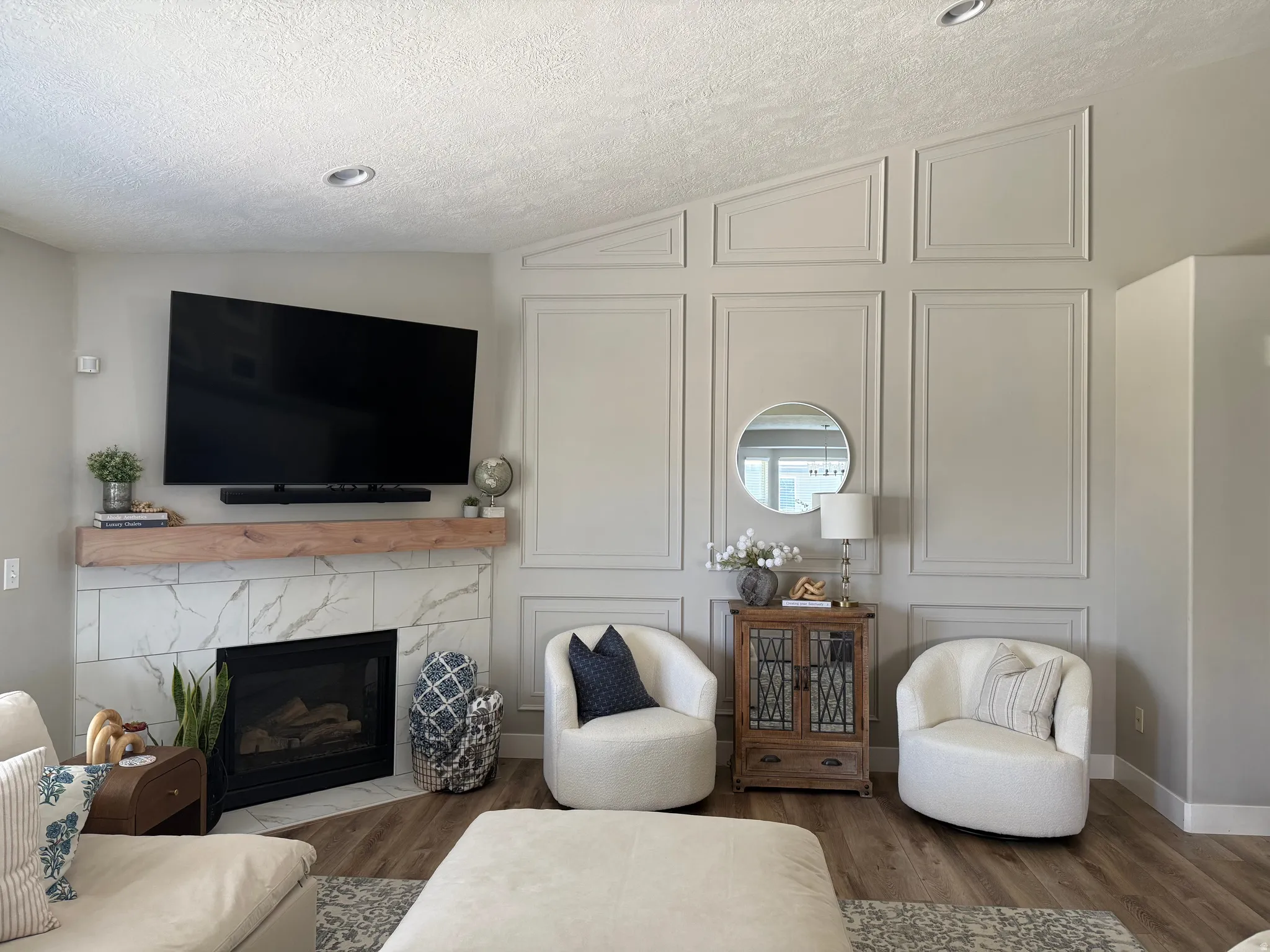 Vaulted ceiling, recessed lighting, fireplace with a wood mantel and marble-look tile surround, wood-finish flooring, and decorative wall paneling