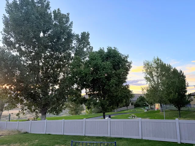 Fenced property line with a manicured lawn, established trees, and open green space beyond