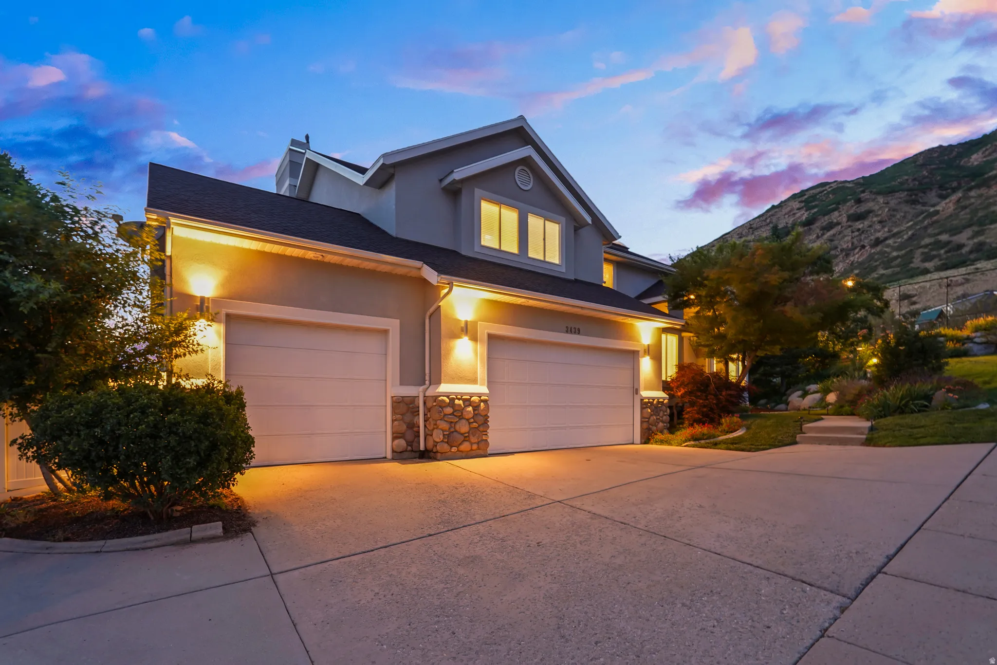 Stucco exterior with stone accents, attached two-car garage, concrete driveway, and established landscaping