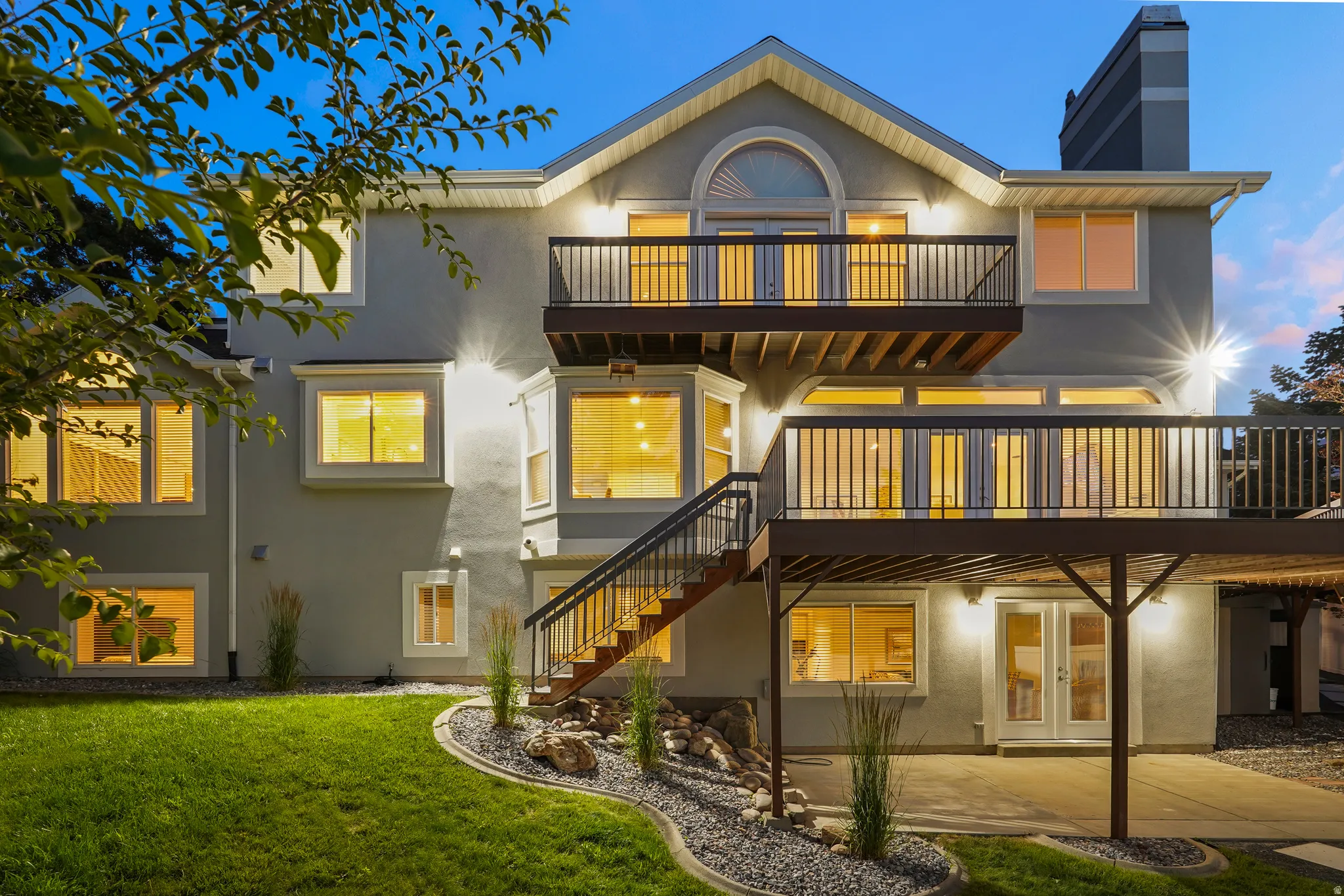 Multi-level decks with dark railings, a lower concrete patio, and landscaped rock beds
