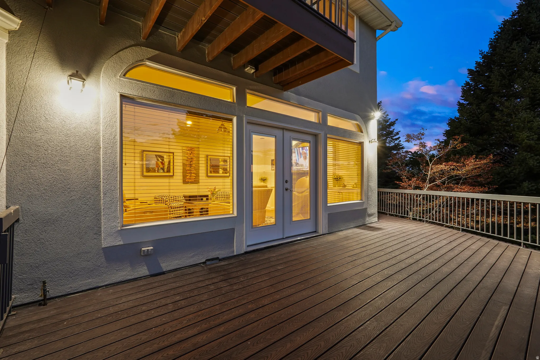 Spacious exterior deck with wood-finish flooring, white railing, and wall-mounted exterior lighting