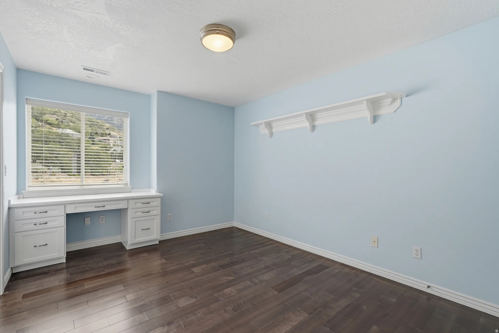 Built-in desk with cabinetry, wood-finish flooring, overhead lighting, and wall-mounted shelving