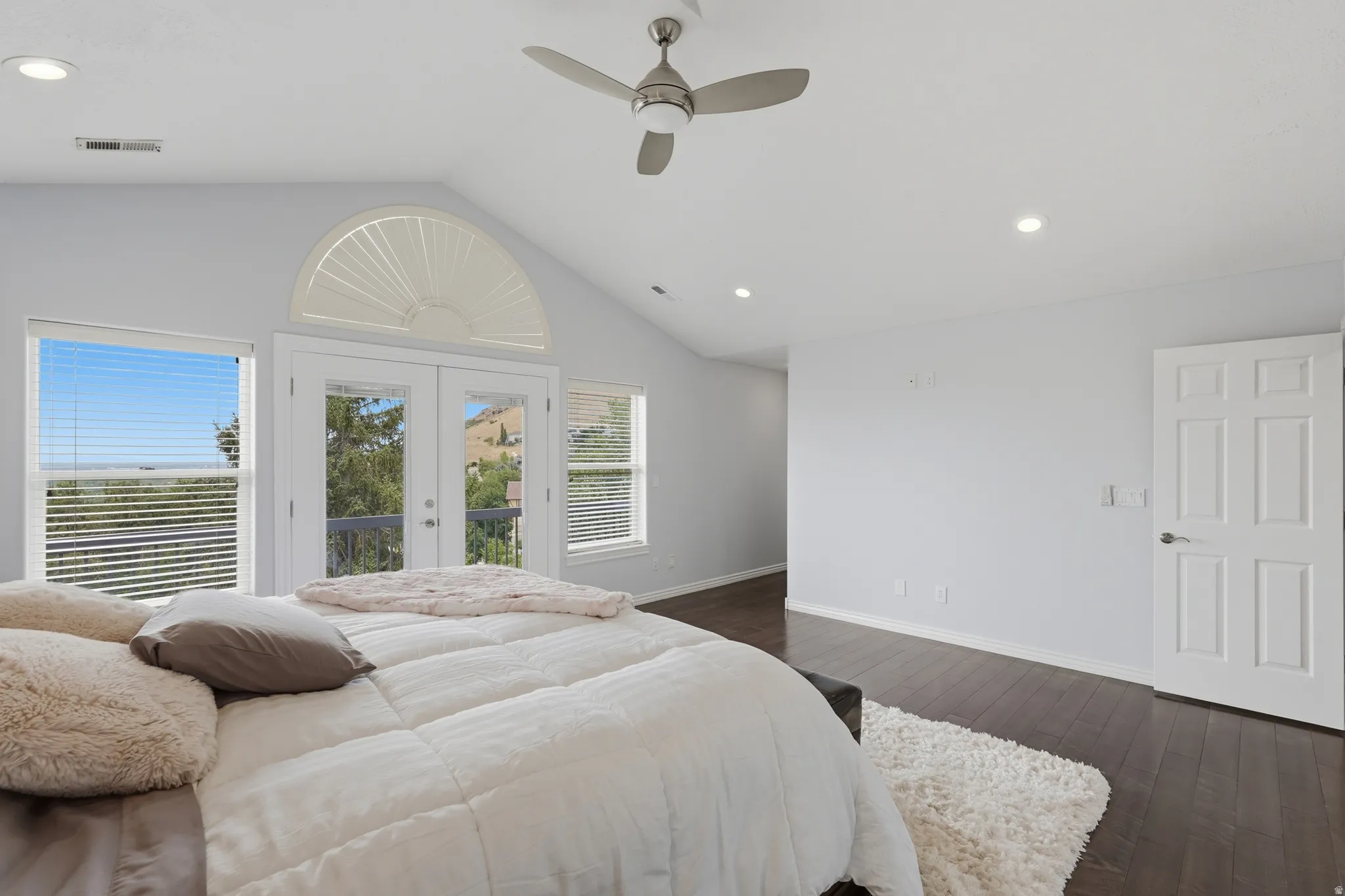 Vaulted ceiling with a ceiling fan and recessed lighting, dark wood-finish flooring, white paneled door, and double glass doors with transom window