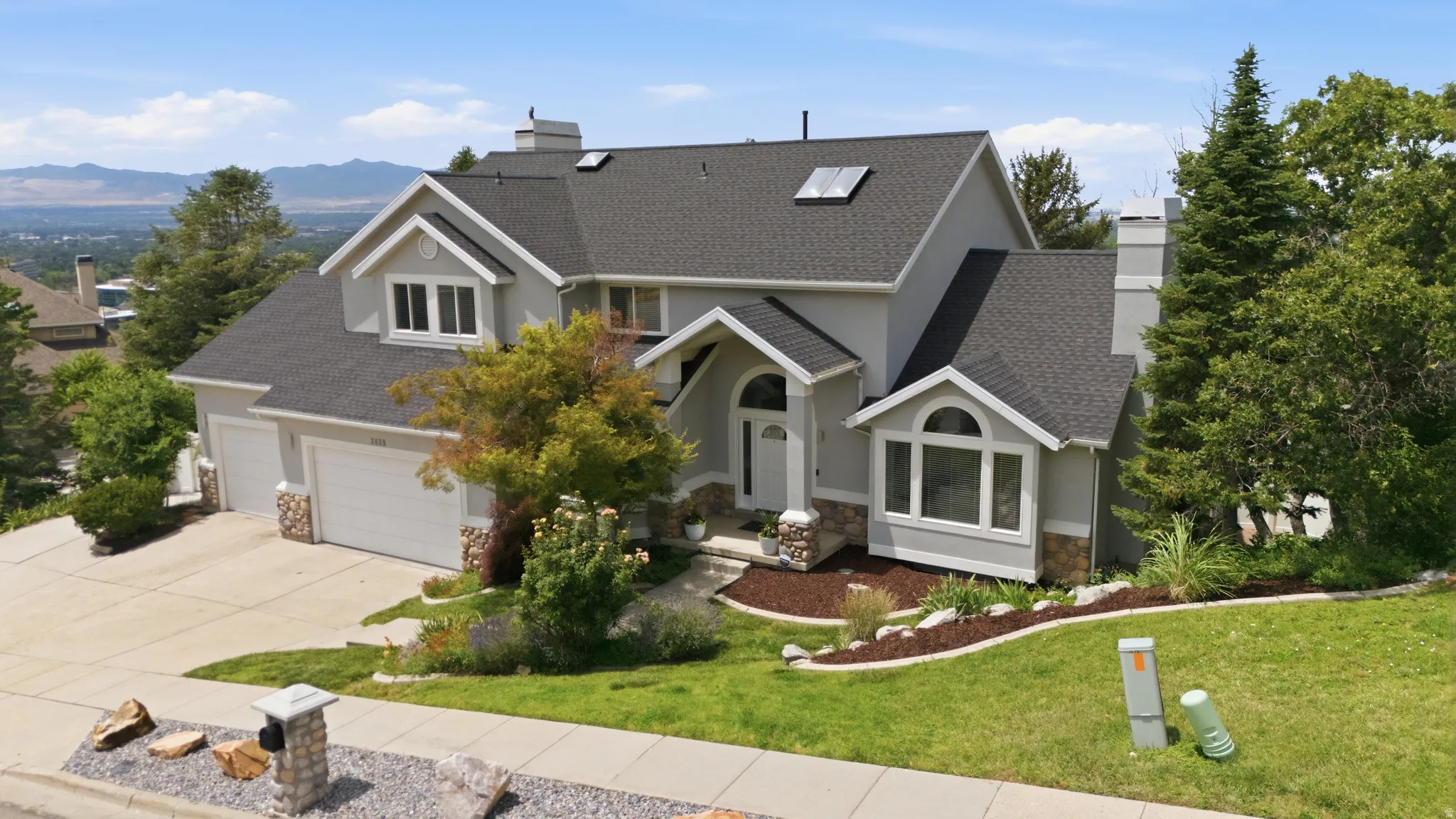Multi-level residence featuring a gray exterior, stone facade accents, and a dark shingle roof