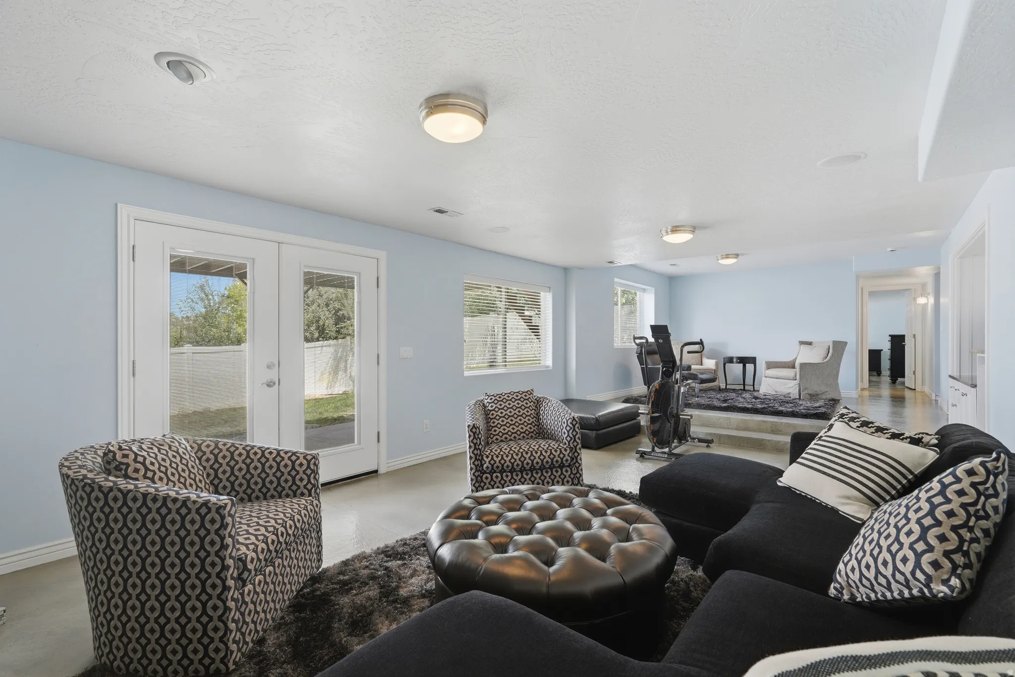 Spacious room featuring light blue walls, multiple windows, and double glass-paneled doors with white trim