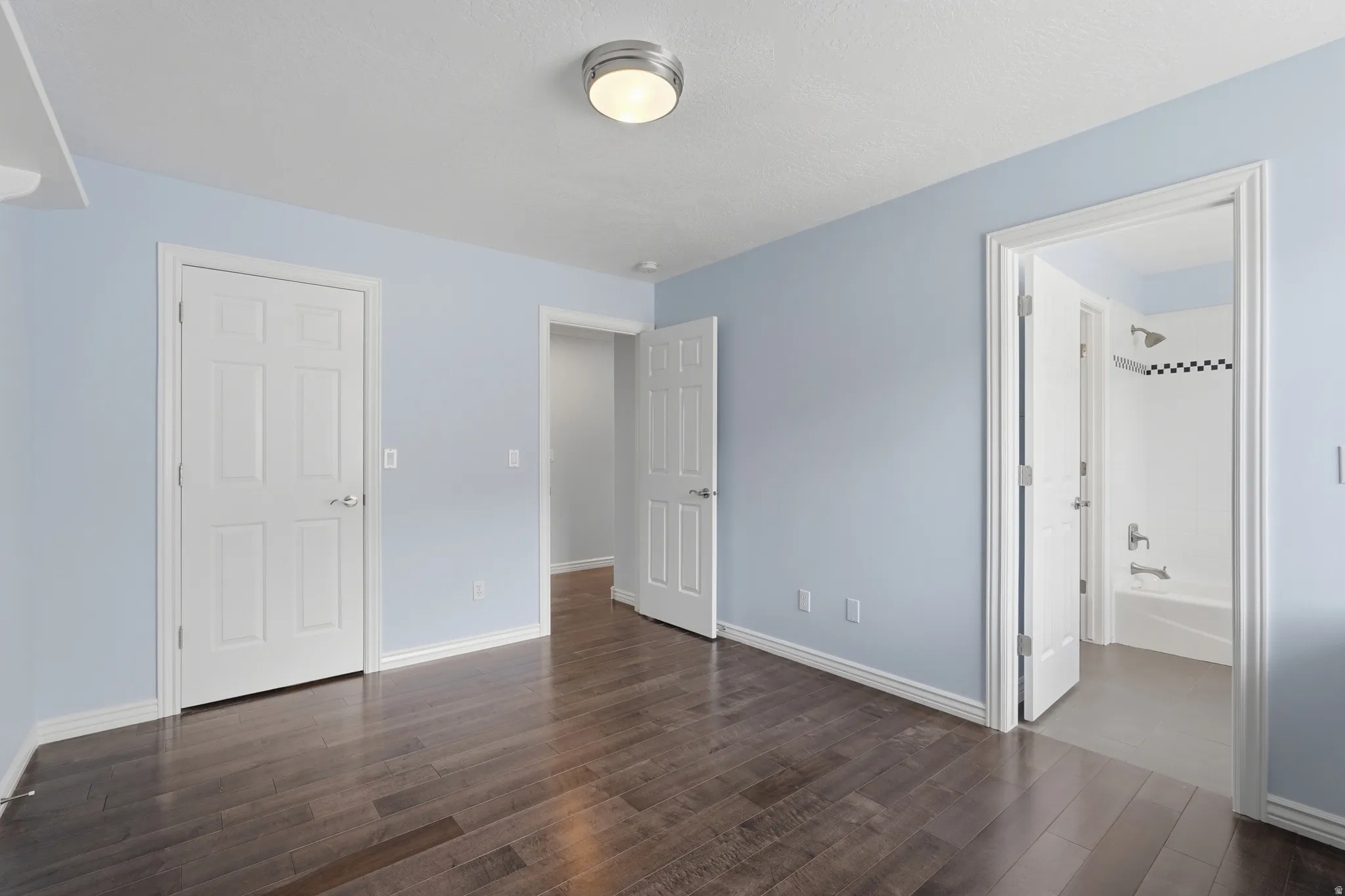 Hardwood-finish flooring, light blue wall paint, white trim, flat ceiling with flush mount lighting, and interior doors