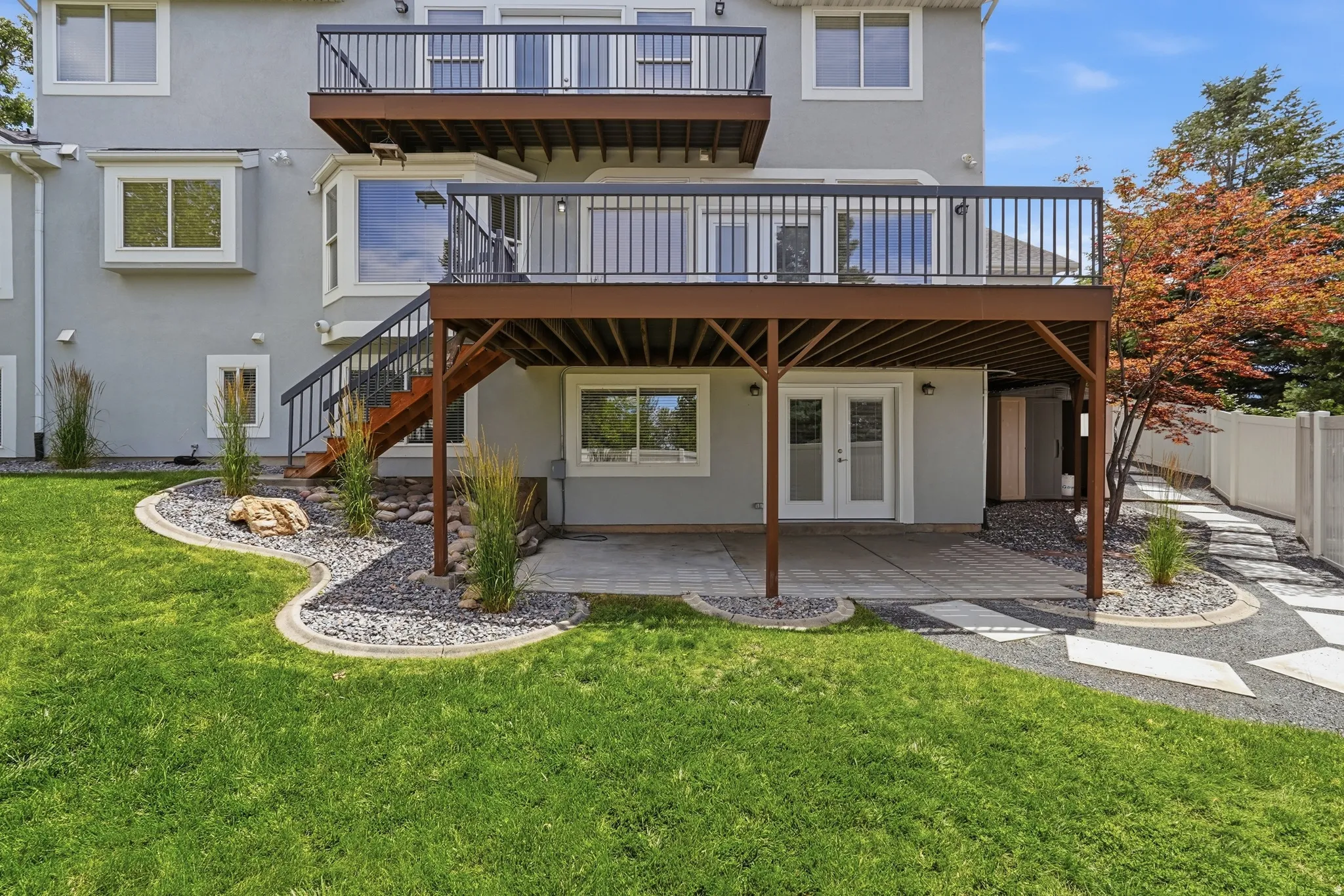 Two-story deck with dark railings, a lower-level patio with double doors, and a manicured lawn