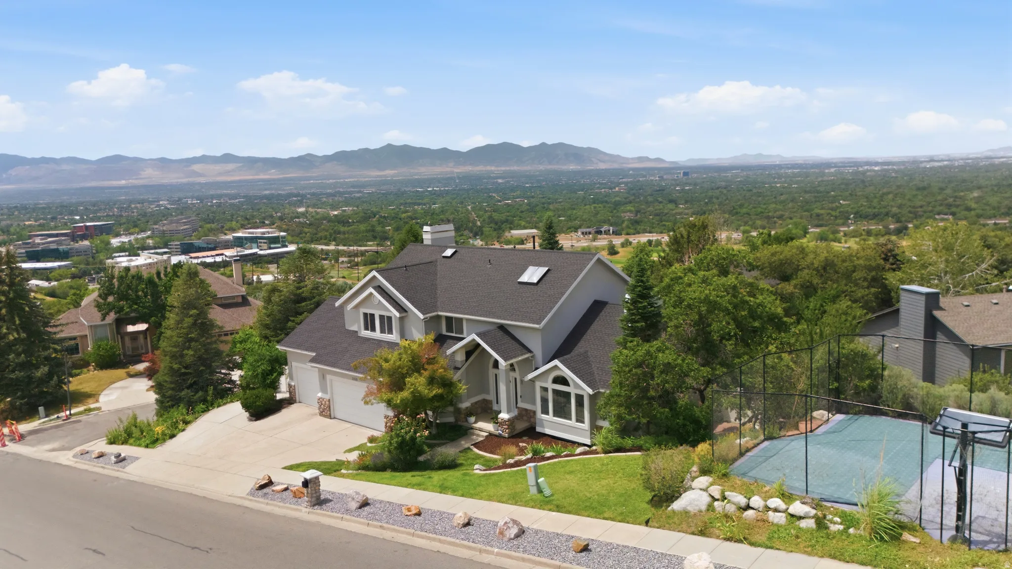 Contemporary residence featuring a paved driveway, attached two-car garage, manicured landscaping, and a fenced sports court