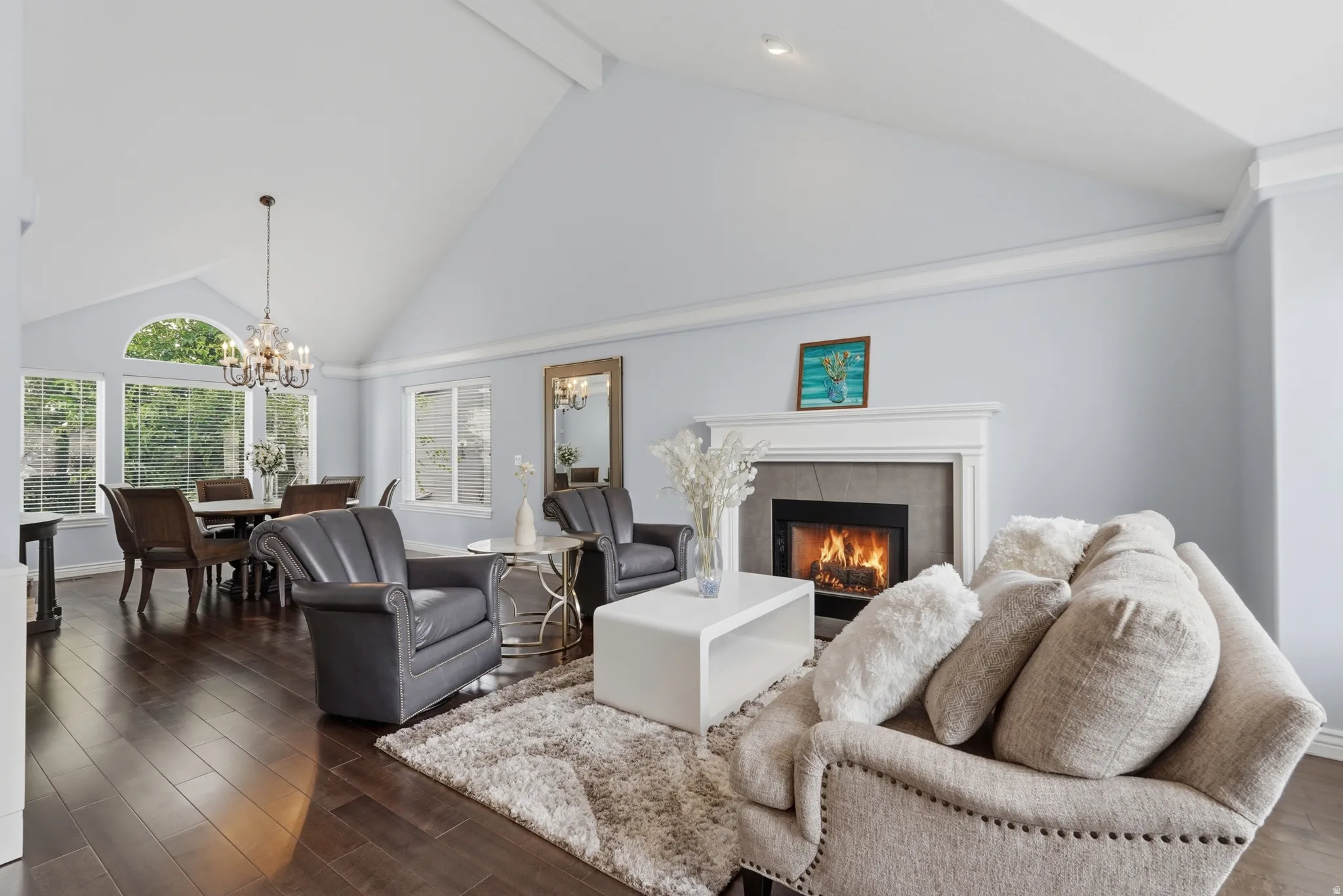 Vaulted ceiling with an integrated chandelier, wood-finish flooring, a fireplace with a stone surround, and an arched window