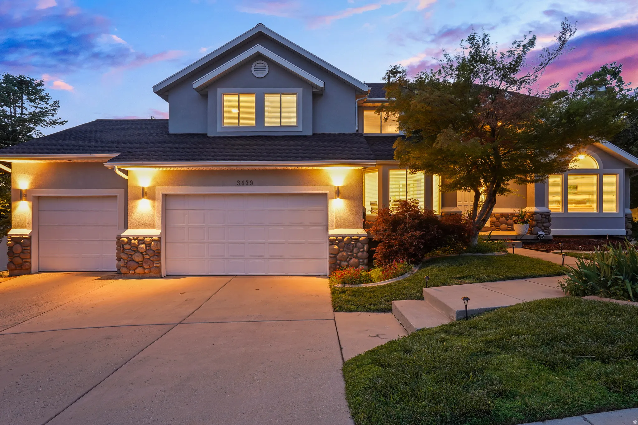 Stucco exterior with stone accents, two-car garage, manicured landscaping, and arched windows