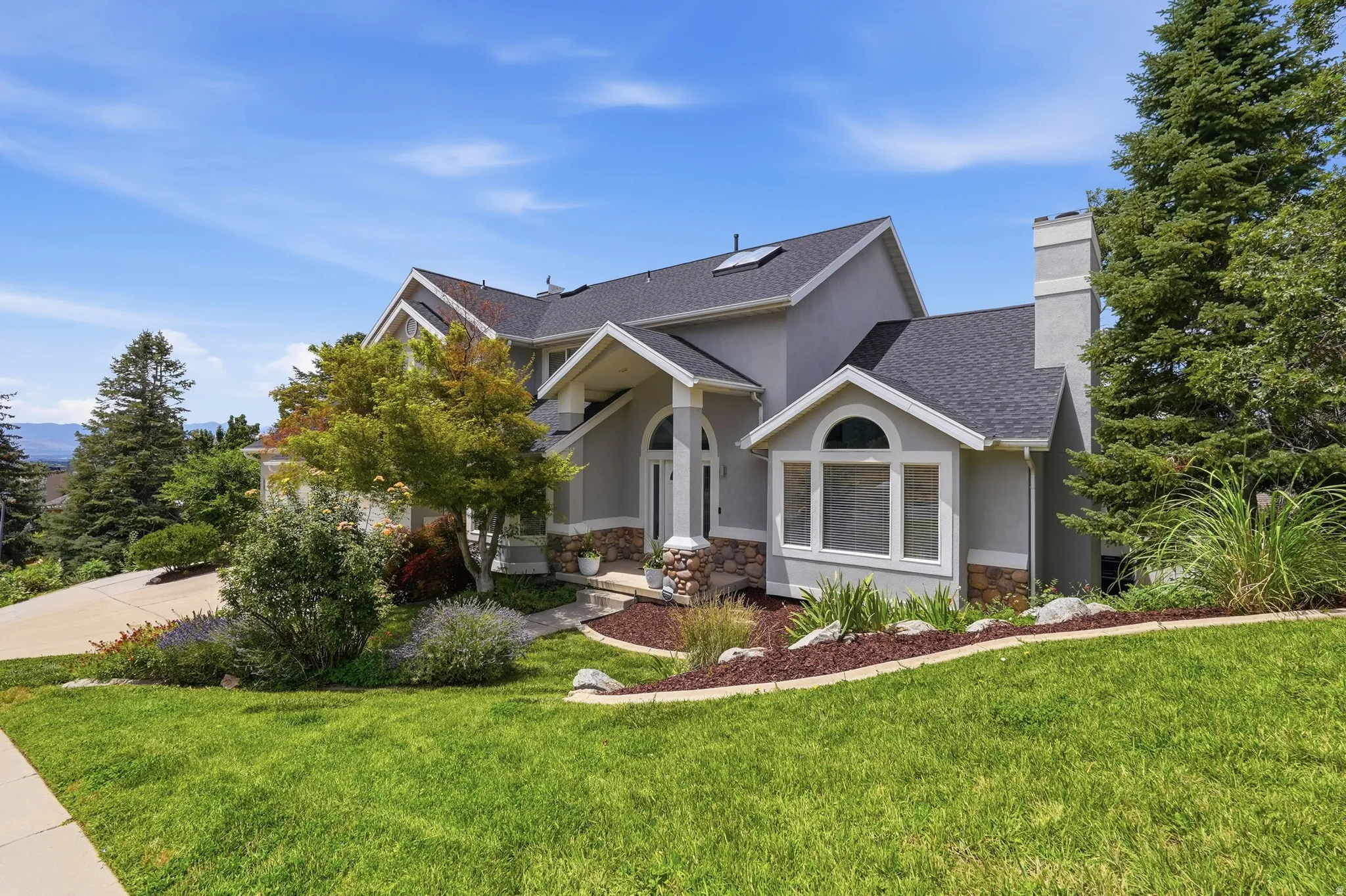 Stucco exterior with stone accents, arched entry, prominent bay window, and gabled roofline