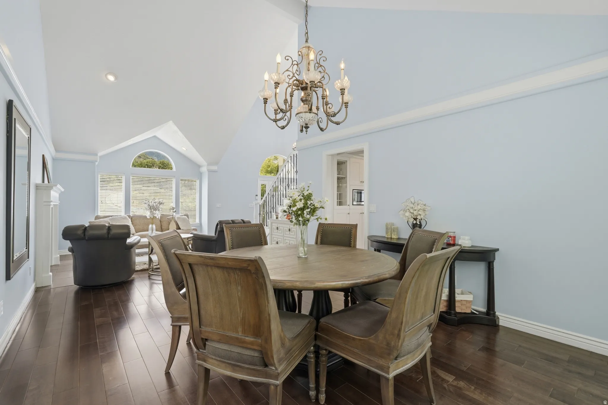 Spacious living area featuring high vaulted ceilings, elegant dark wood-finish flooring, a decorative chandelier, and a prominent arched window