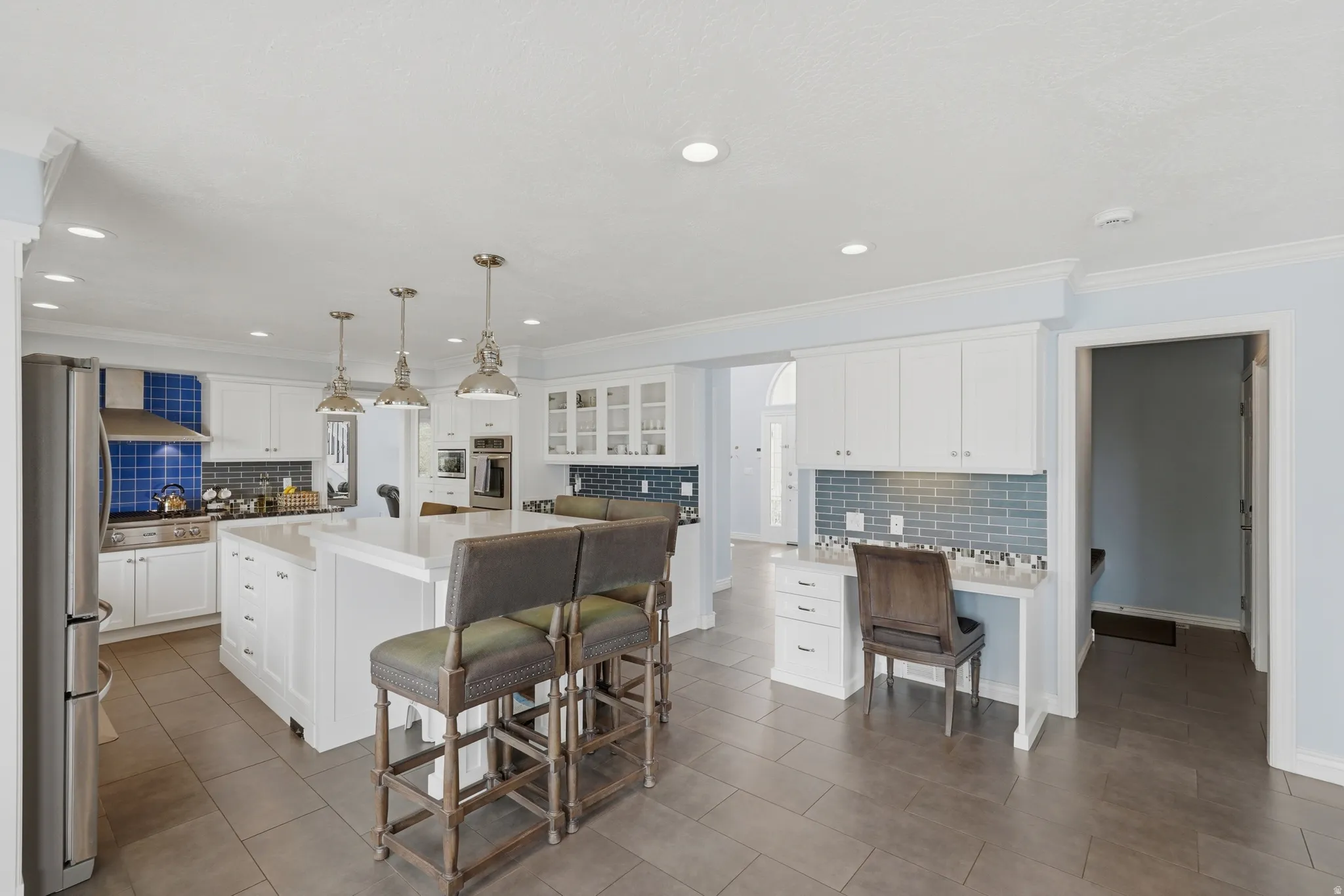 Spacious kitchen featuring an expansive central island, white cabinetry, integrated stainless steel appliances, tile flooring, and recessed lighting
