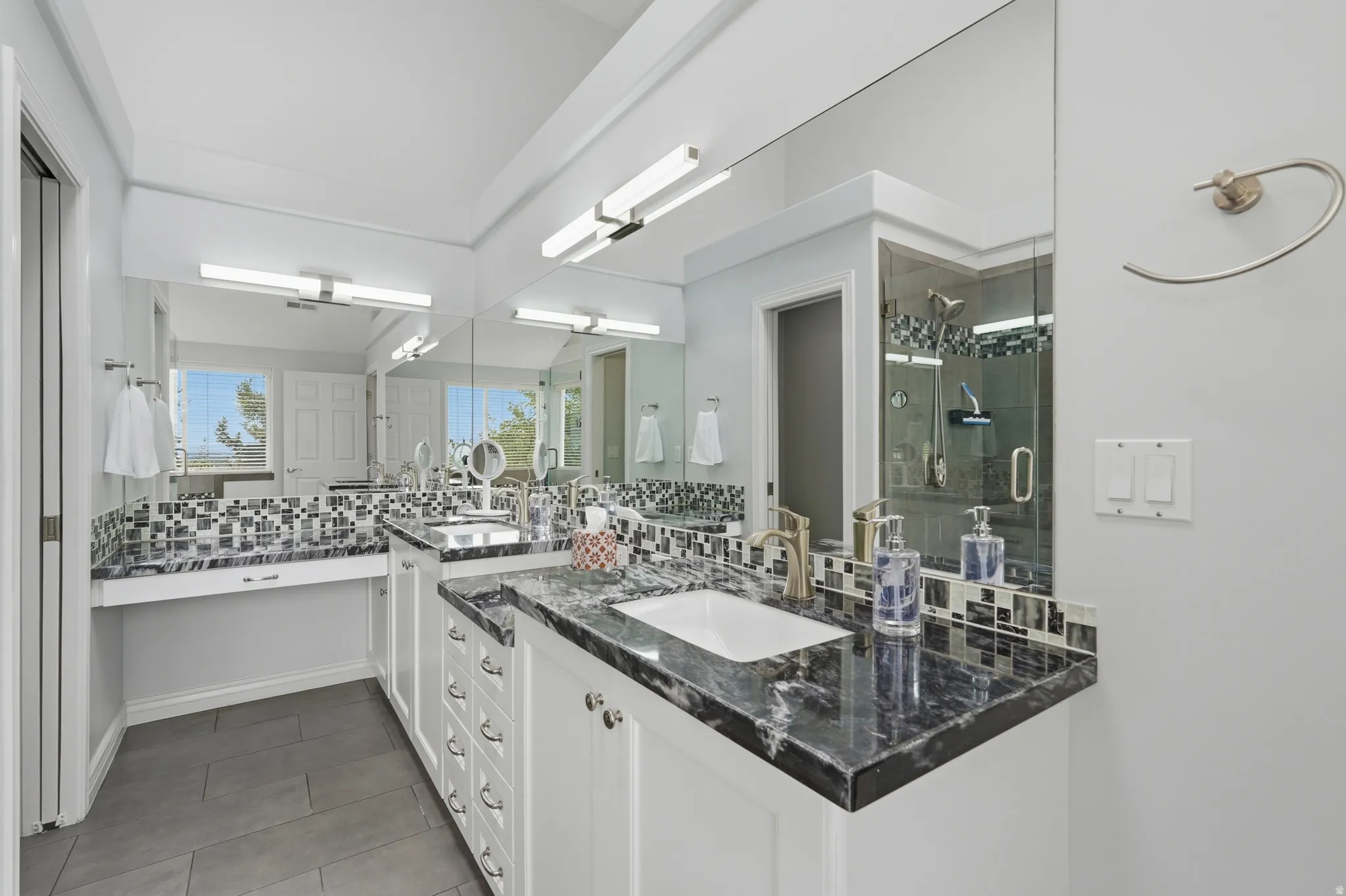 Dual vanity with dark stone countertops, under-mount sinks, and mosaic tile backsplash