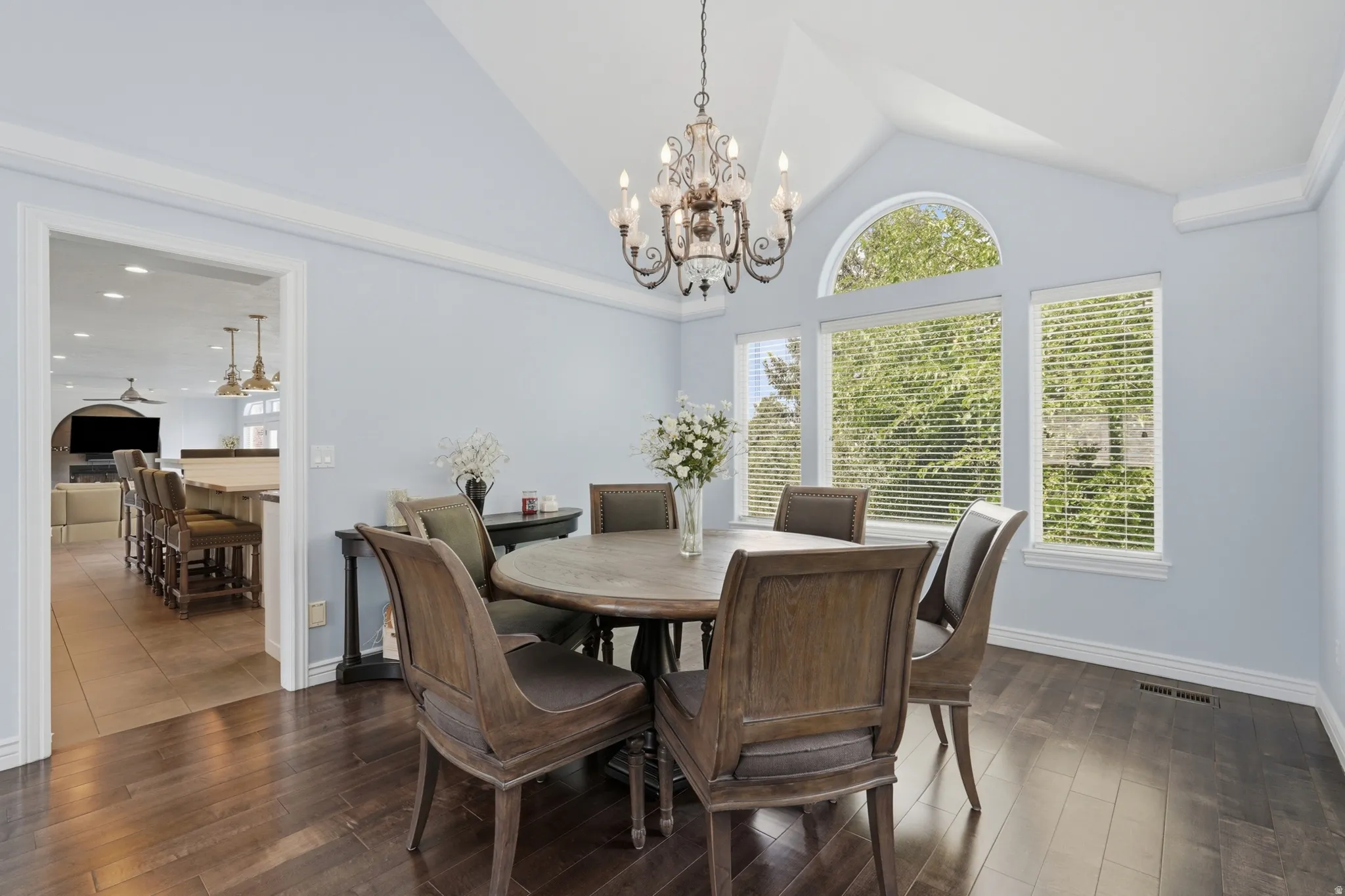 Vaulted ceiling with an ornate chandelier, dark wood-finish flooring, and multiple large windows with an arched transom