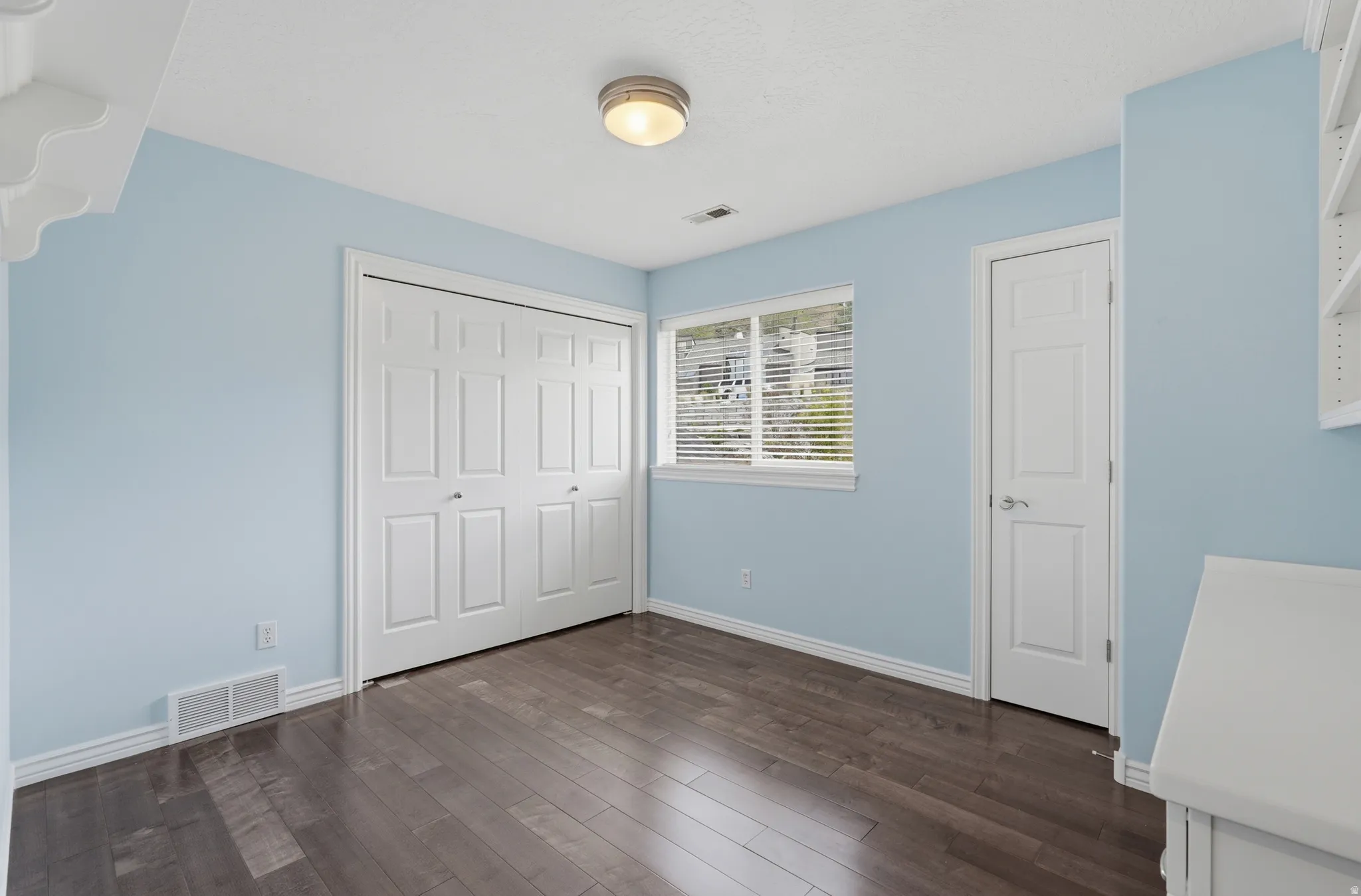 Wood-finish flooring, white trim, and a window with horizontal blinds provide natural light