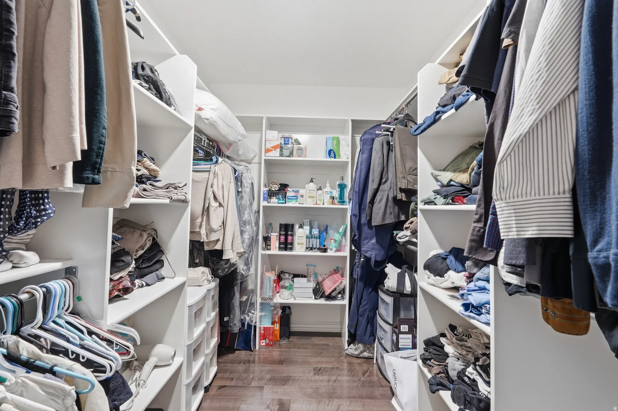 Walk-in closet featuring built-in white shelving, hanging rods, and wood-finish flooring