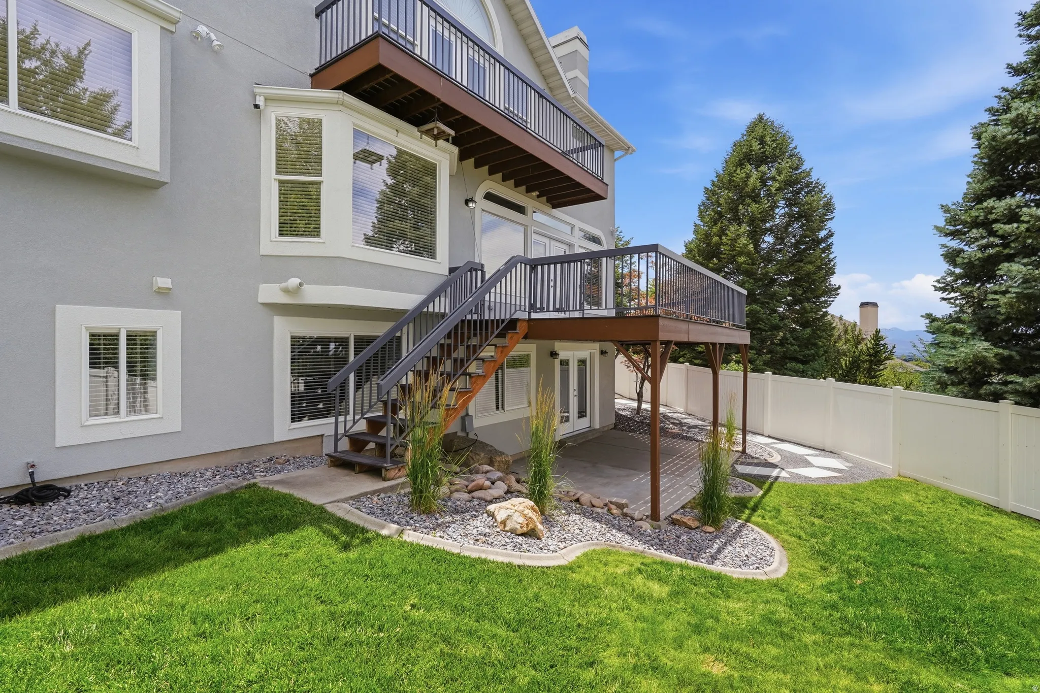 Exterior featuring a private deck, a lower patio, a manicured lawn, and a white privacy fence