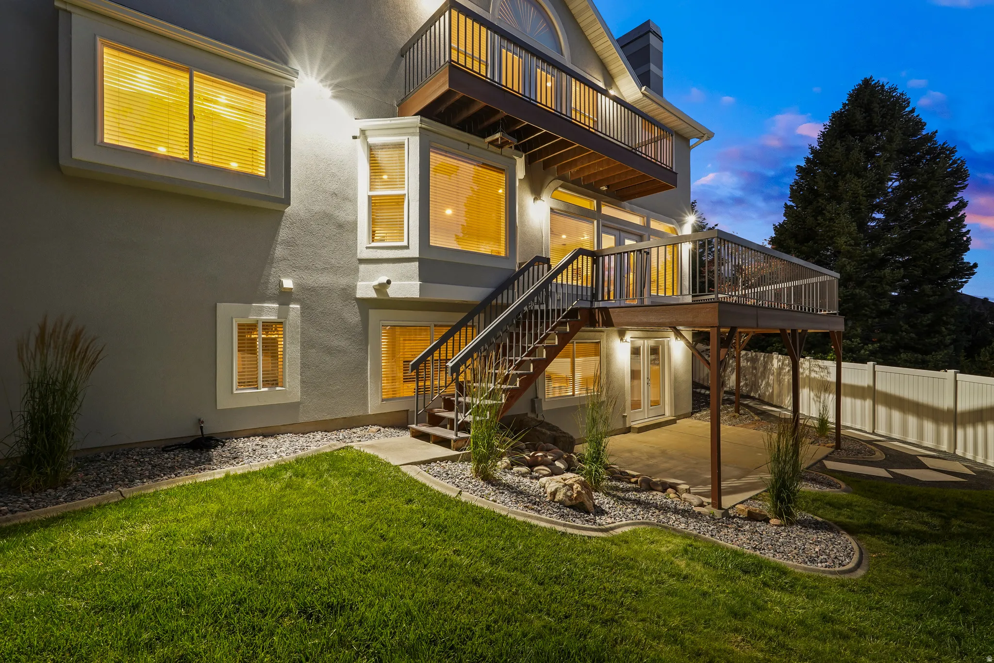 Multi-level exterior with stucco finish, upper-level balcony, lower-level deck, and a concrete patio