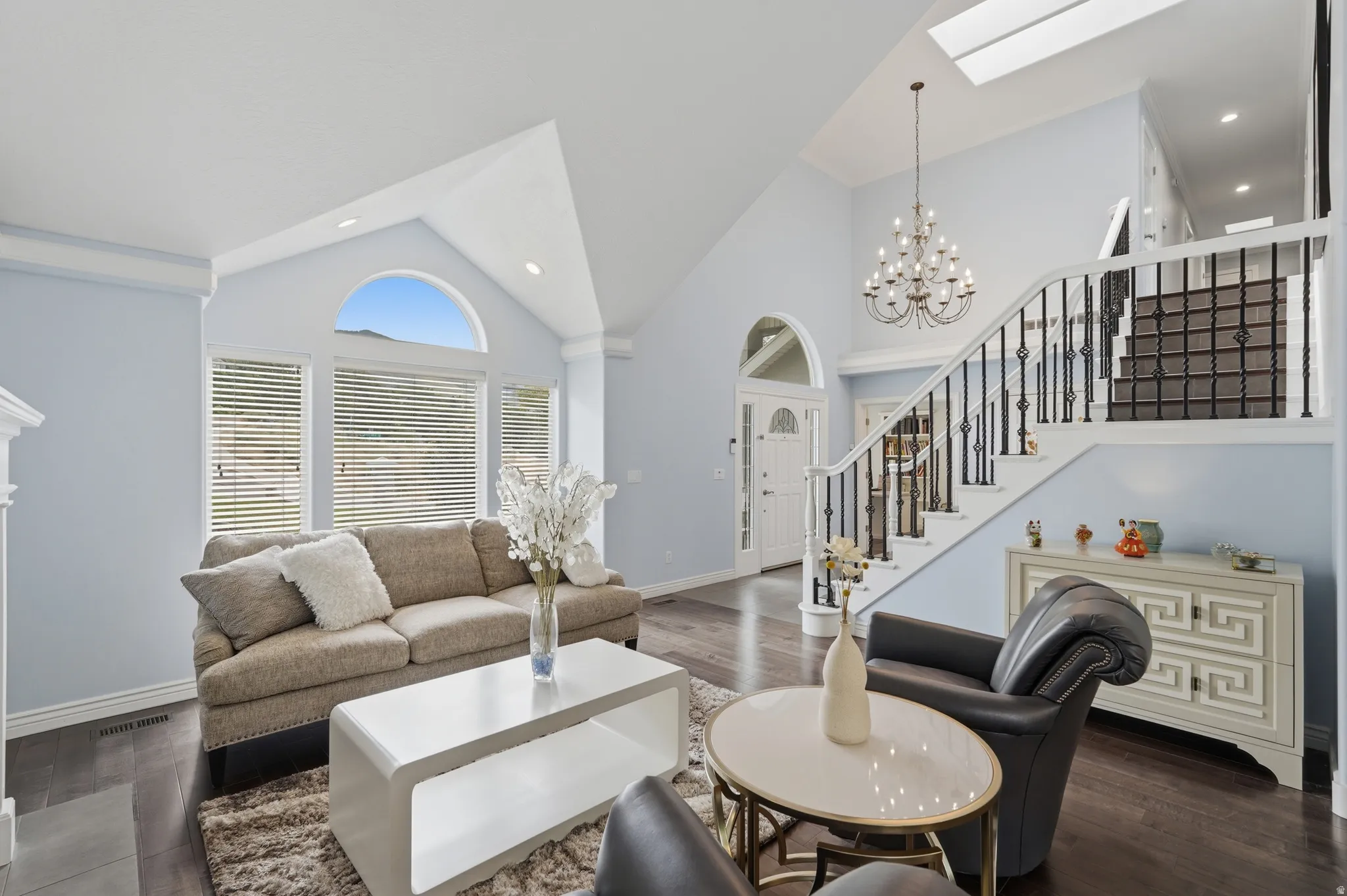 Vaulted ceilings, wood-finish flooring, arched windows, skylight, and a decorative staircase