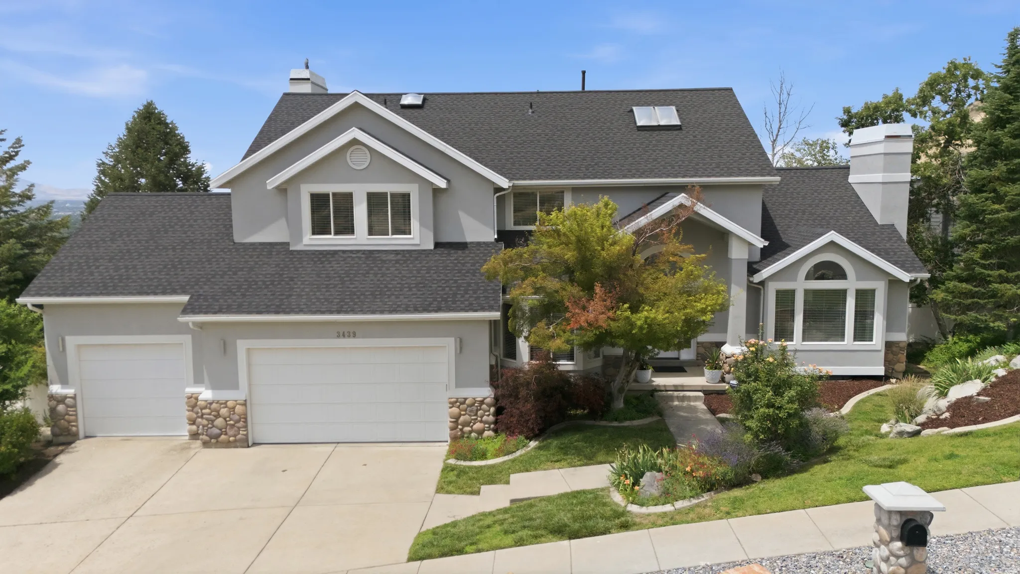 Multi-level exterior with light gray stucco and stone accents, featuring a two-car garage and an additional single-car garage
