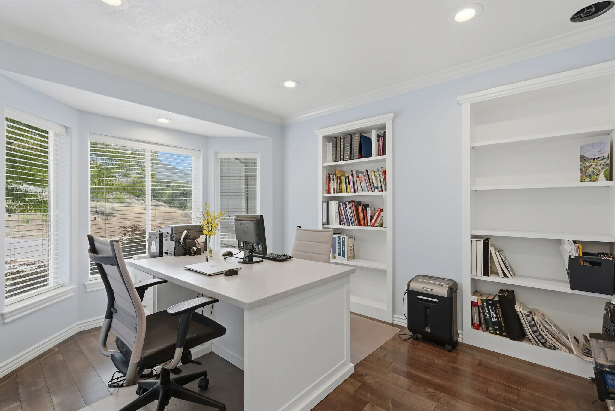 Bay window with natural light, rich wood-finish flooring, recessed ceiling lighting, and built-in shelving units